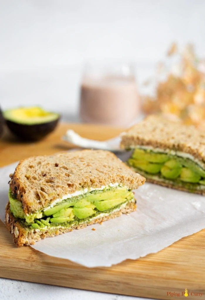 Avocado sandwich on a cutting board with a smoothie in the back