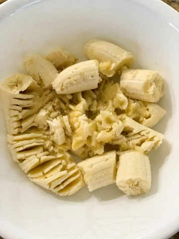 Bananas in a white bowl being mashed