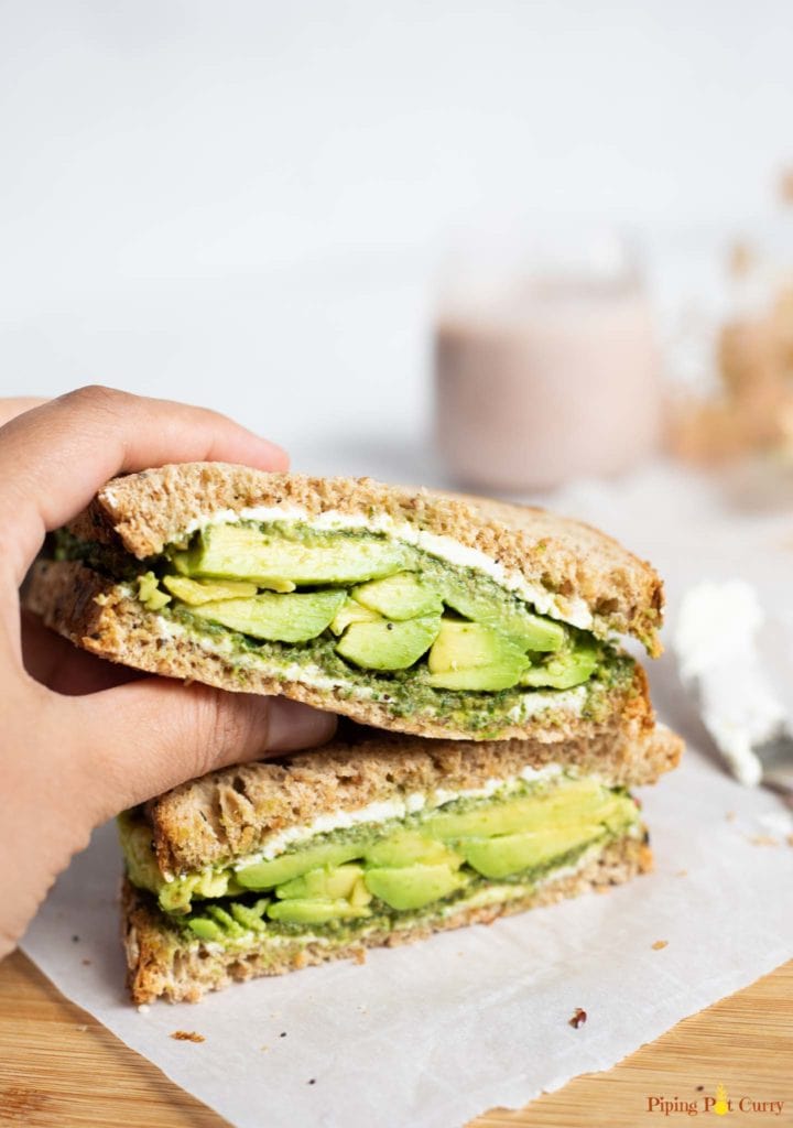 Sandwich with avocado, chutney and cream cheese being picked to be eaten