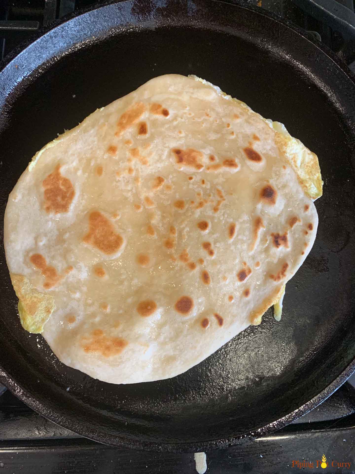 Paneer Kathi Roll base - Piping Pot Curry A flatbread being cooked on a pan