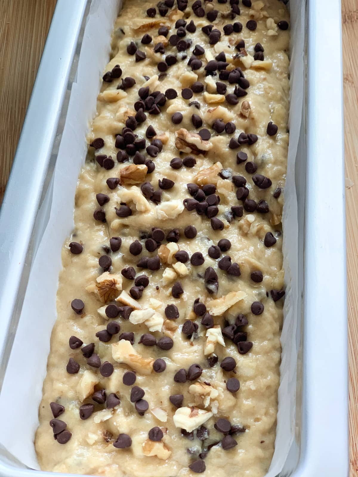 Batter in a bread baking pan, topped with chopped walnuts and chocolate chips 