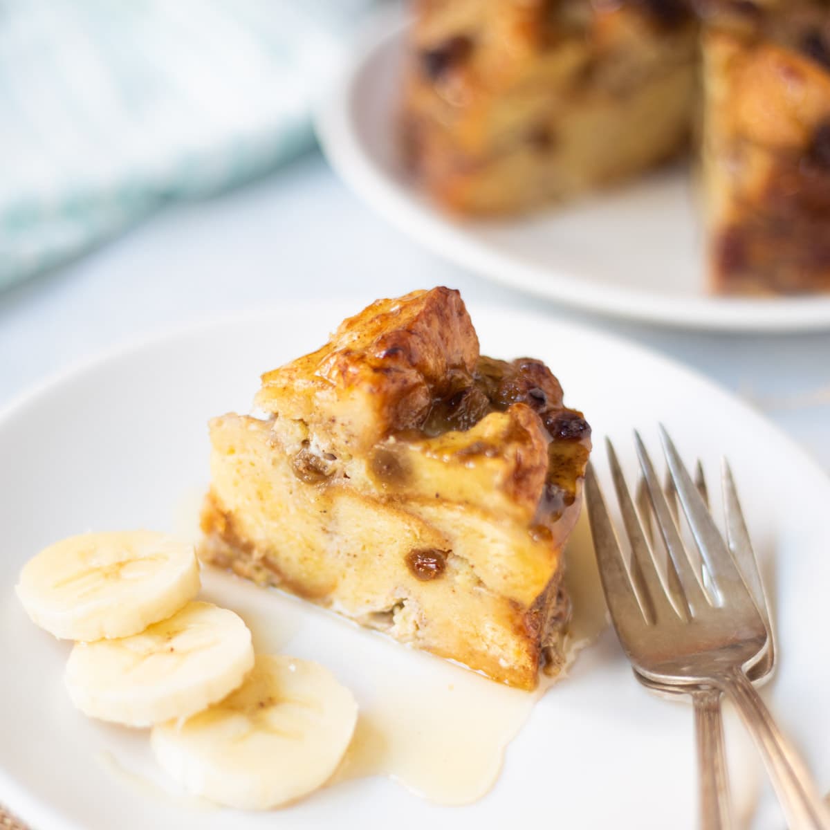 bread pudding drizzled with syrup and sliced banana on the side.