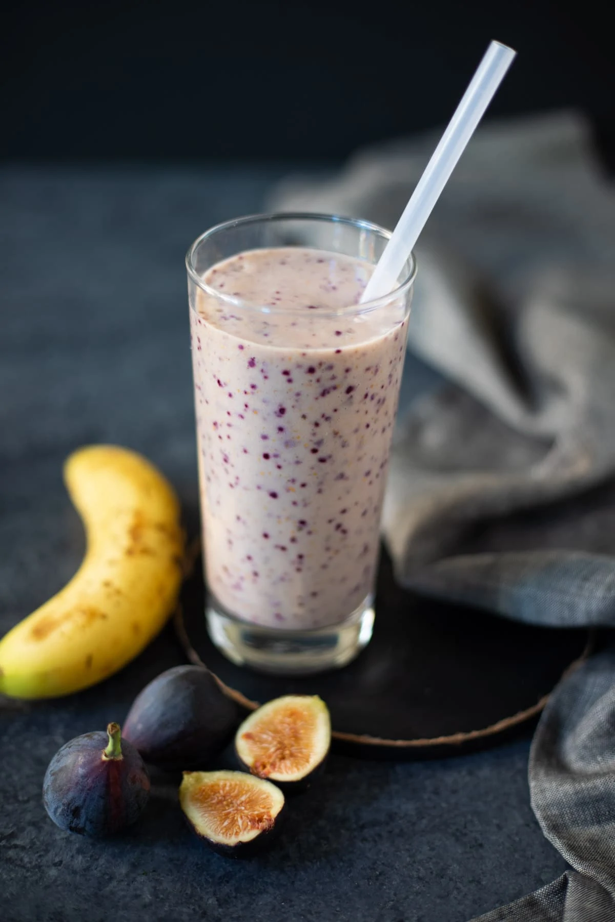 A glass of smoothie with the ingredients such as banana and figs around it 