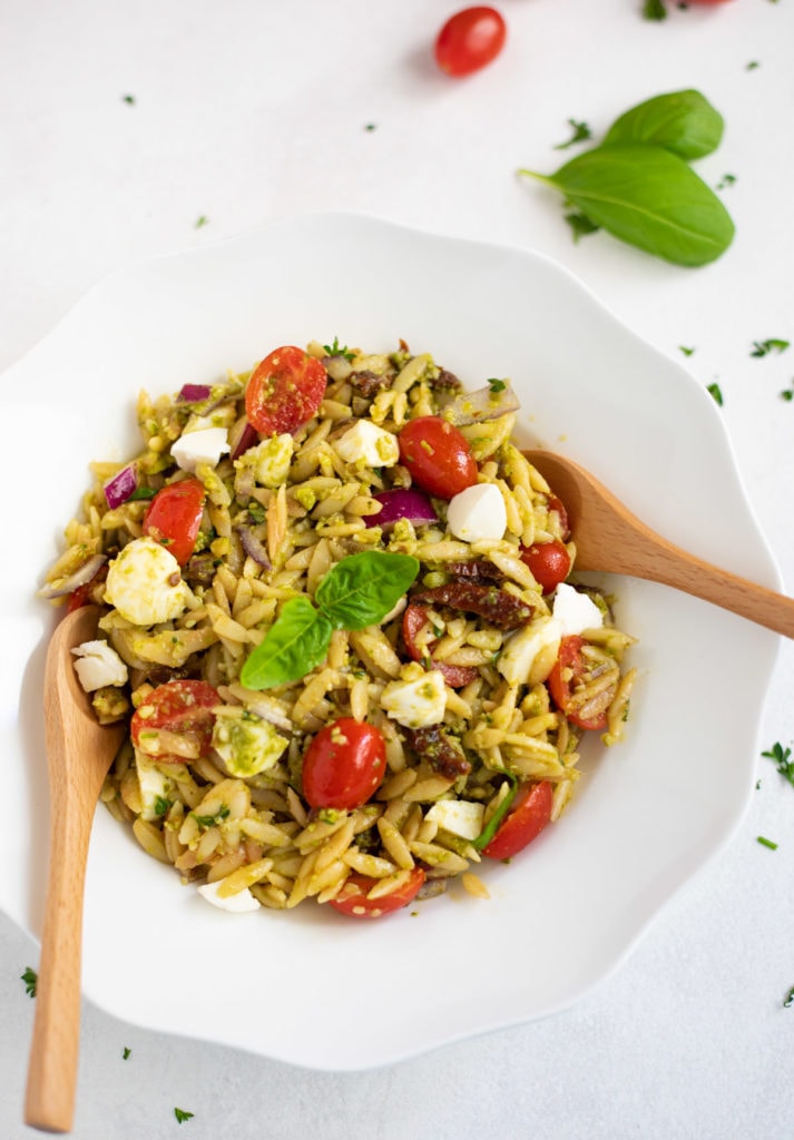 Pesto orzo pasta salad with tomatoes and mozzarella garnished with basil leaves