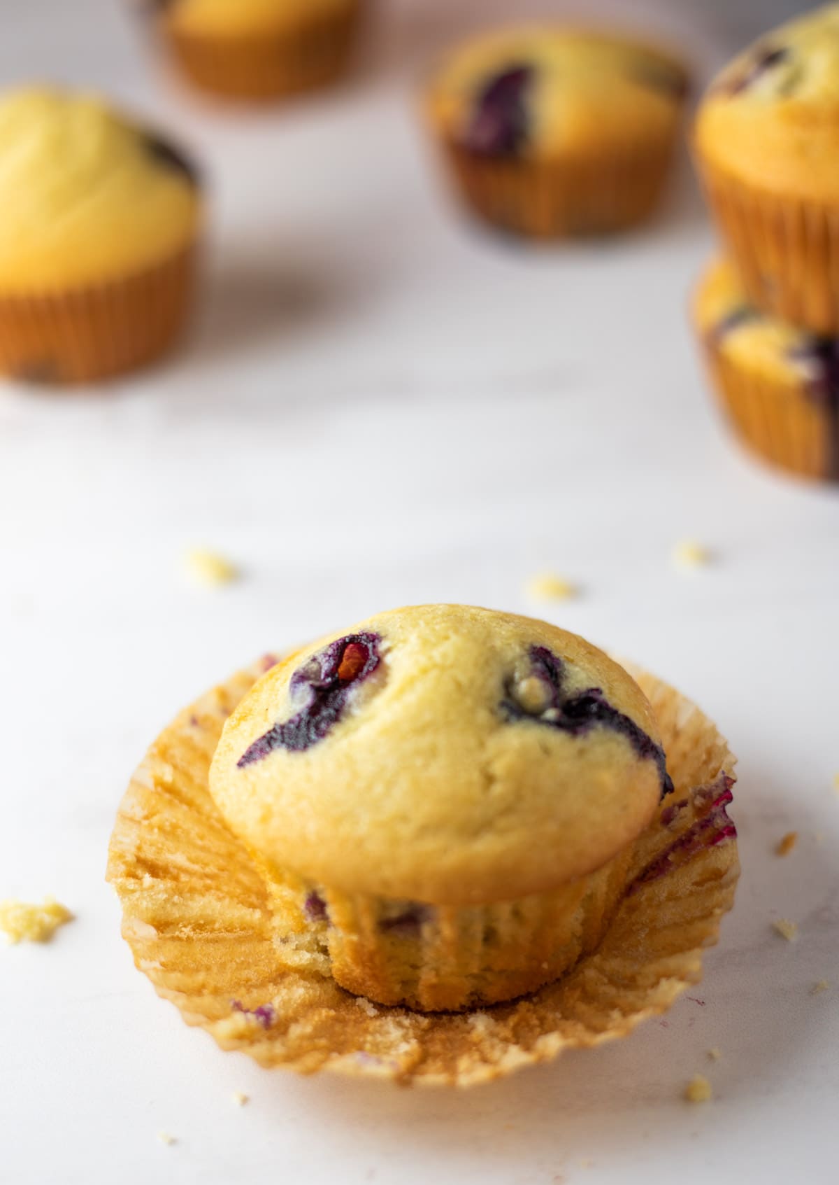 Blueberry muffin with the liner removed and lot of muffins in the back