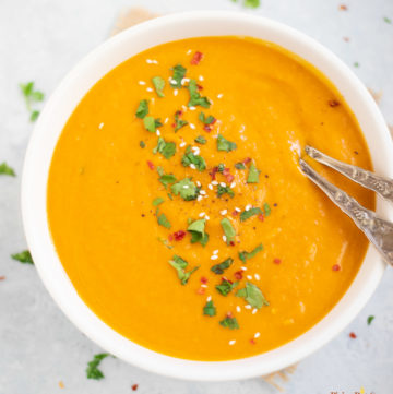 Creamy Carrot Soup in a white bowl garnishes with cilantro, red pepper flakes and sesame seeds