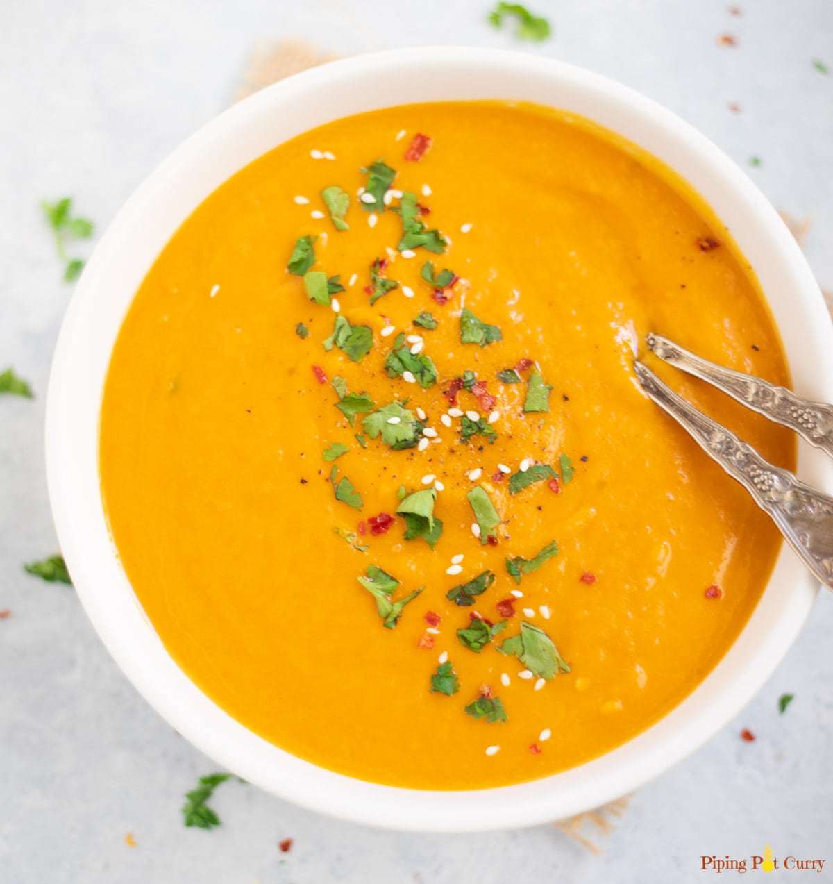 Creamy Carrot Soup in a white bowl garnishes with cilantro, red pepper flakes and sesame seeds