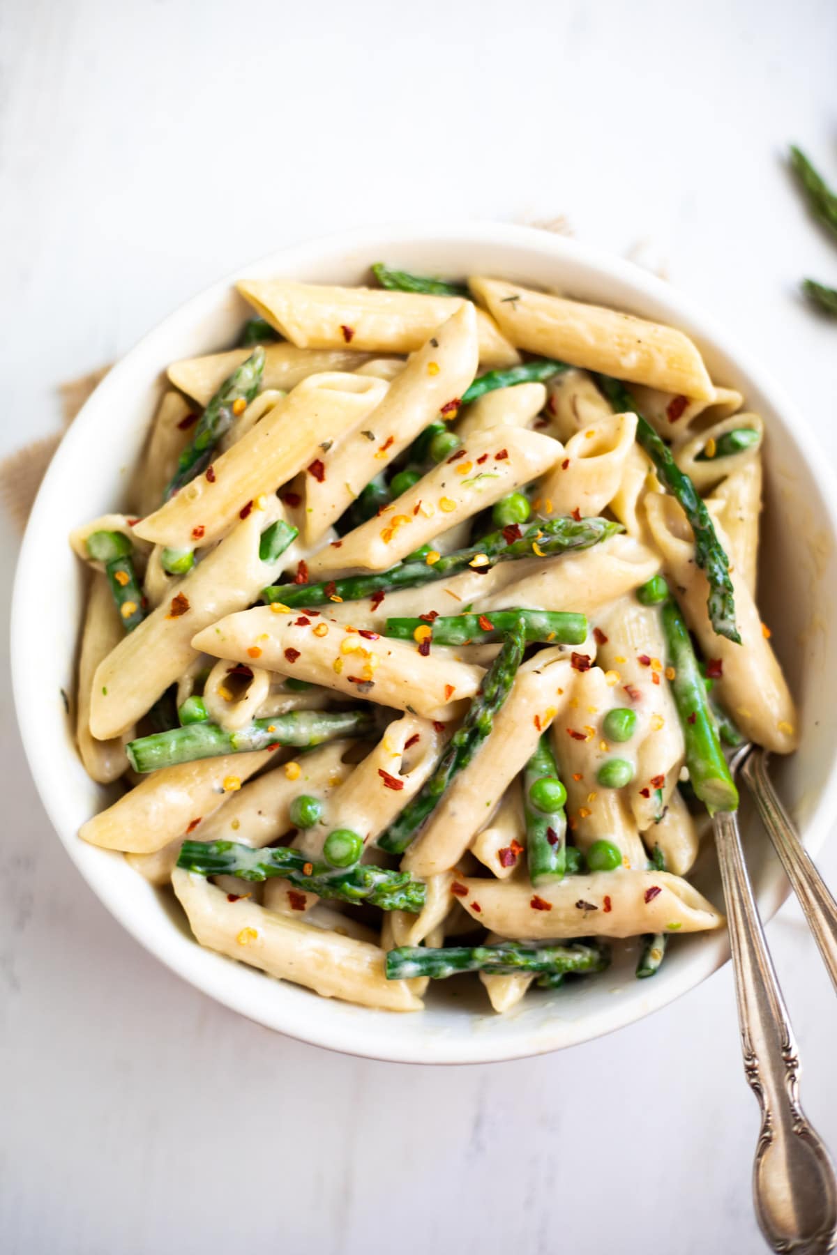 Creamy Asparagus pasta in a white bowl garnished with red chili flakes