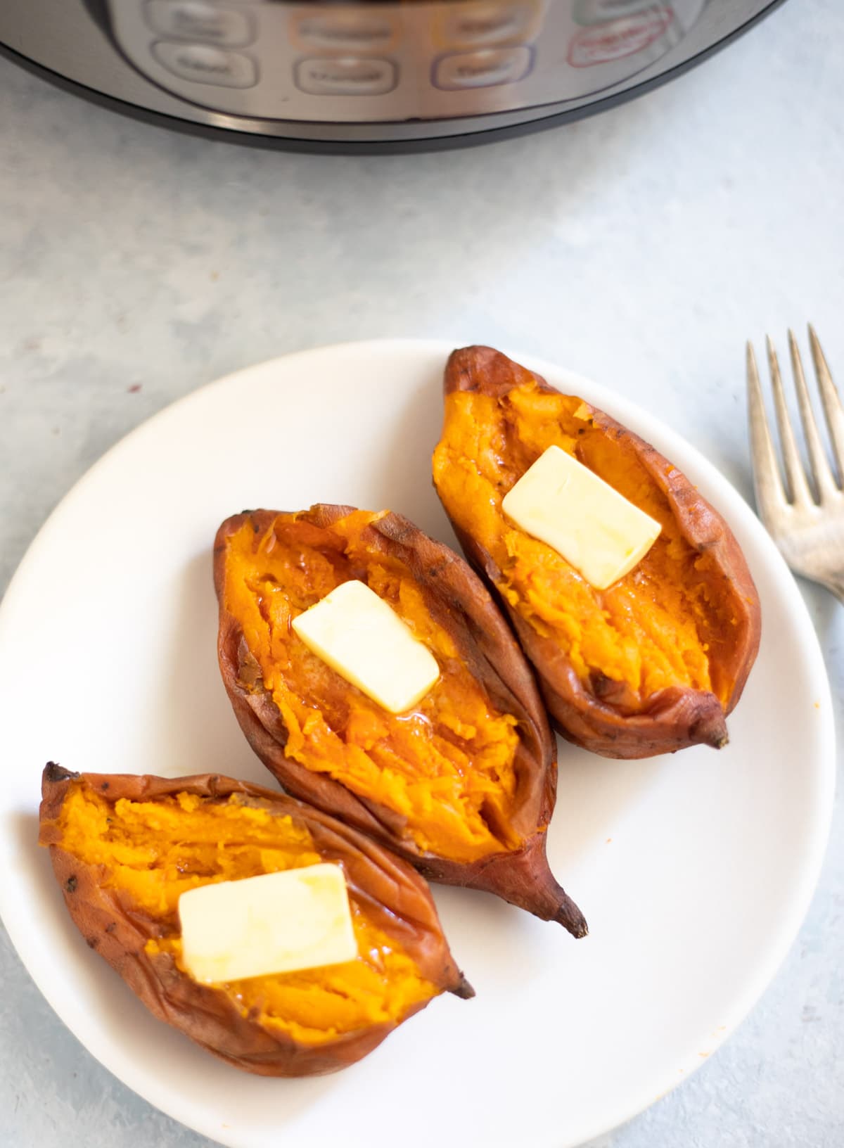 Creamy Sweet potatoes topped with butter in a white plate ion front of the instant pot