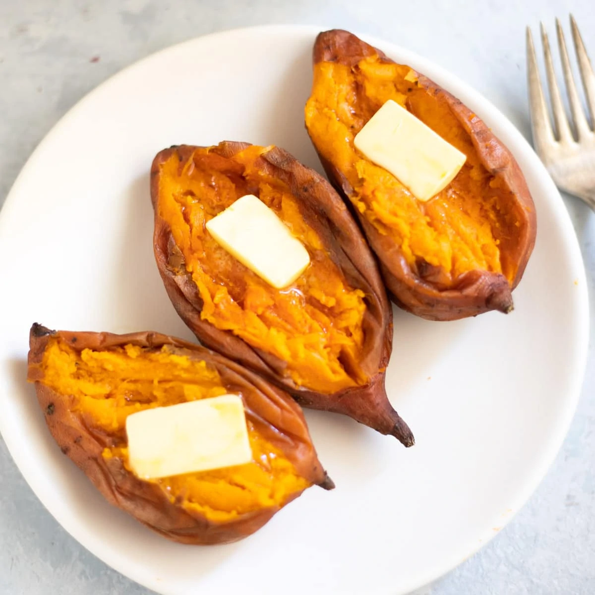 Creamy Sweet potatoes topped with butter in a white plate ion front of the instant pot