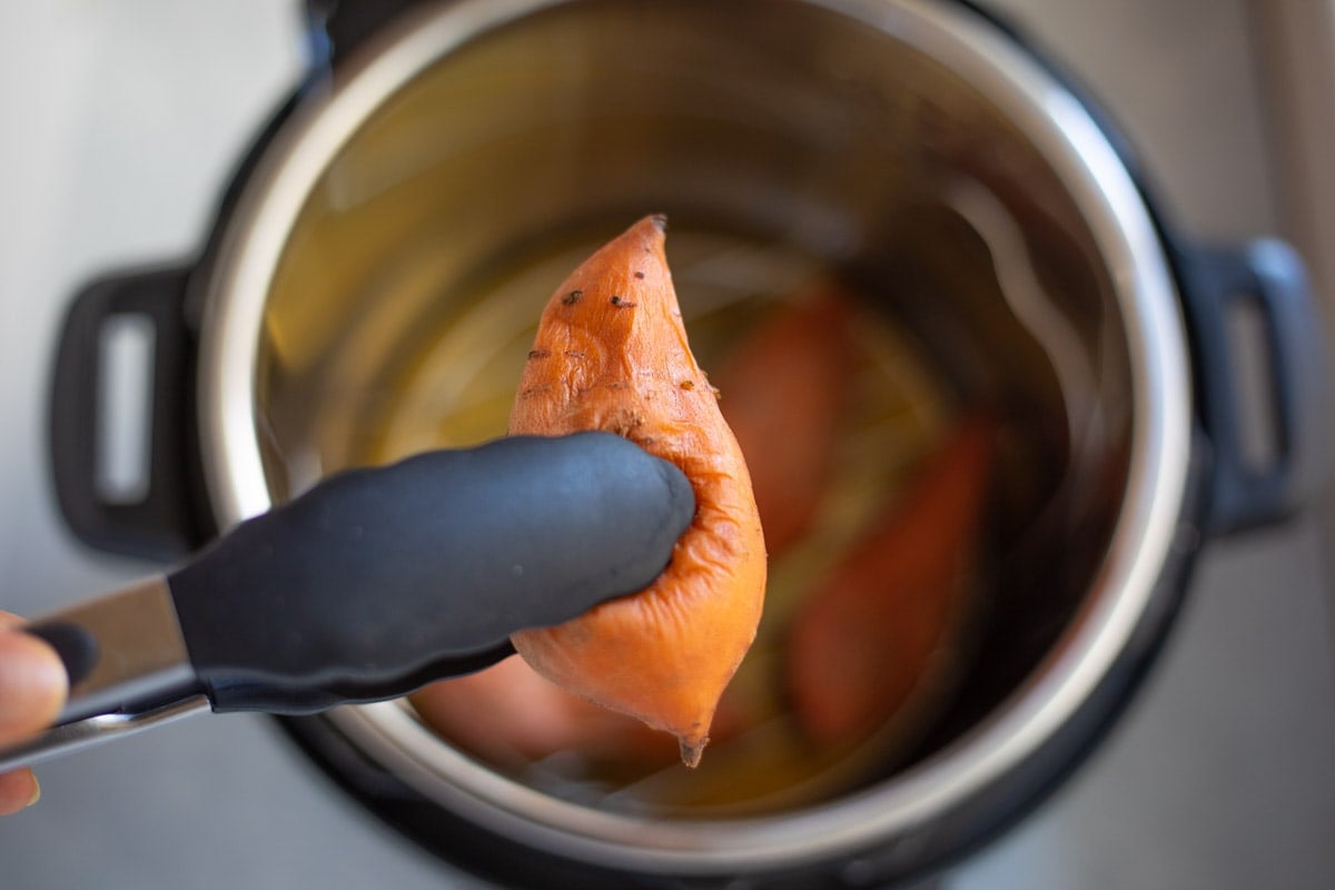 A cooked sweet potato being picked out of the instant pot with tongs 