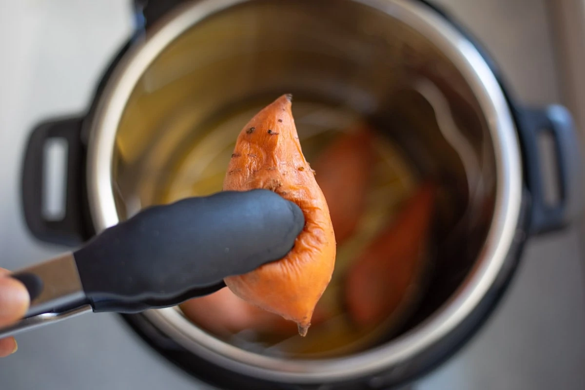 A cooked sweet potato being picked out of the instant pot with tongs