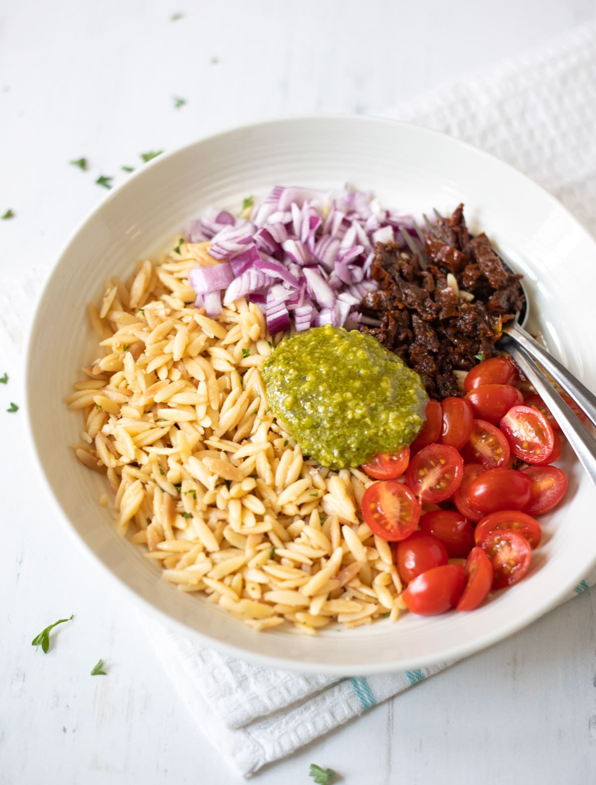 ingredients in a bowl to make salad such as orzo, tomatoes, onions and pesto