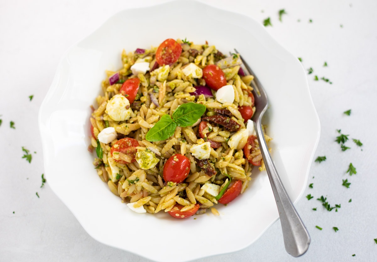 Pesto Orzo pasta salad in a white bowl with a fork