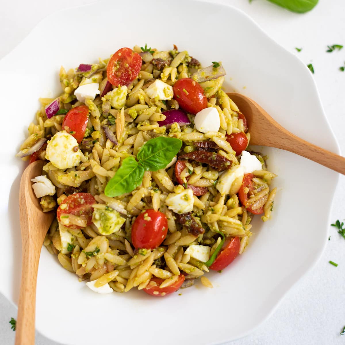 Pesto orzo pasta salad with tomatoes and mozzarella garnished with basil leaves