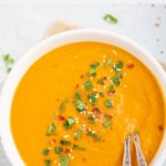 Creamy Vegan Carrot Ginger Soup garnishes with cilantro, red pepper flakes and sesame seeds
