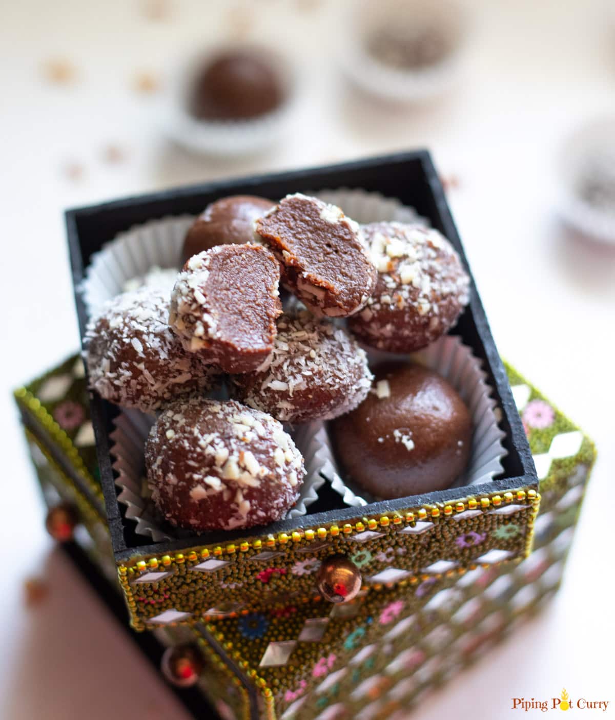 A cut chocolate truffle over other balls in a small decorated box 