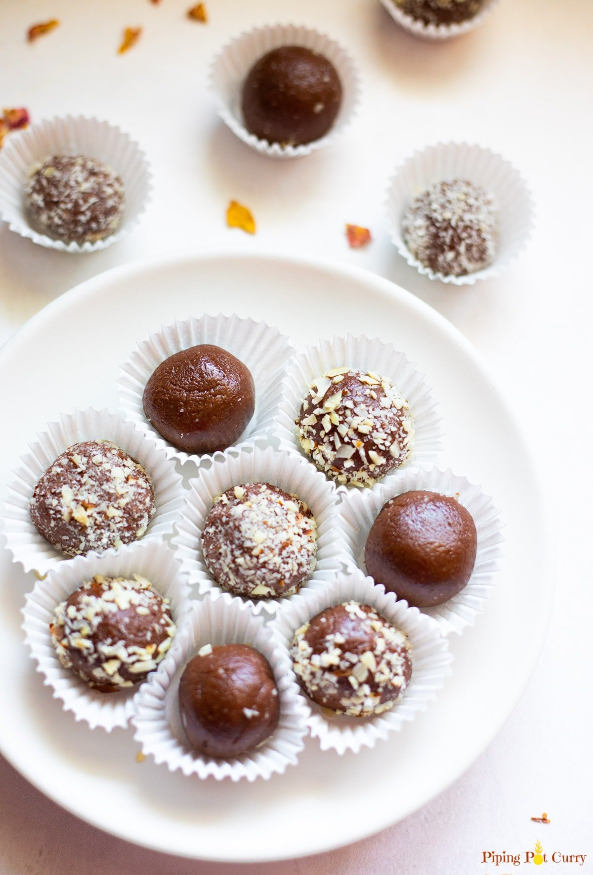 Chocolate balls covered in some chopped nuts in a white plate and spread around.