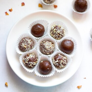 Chocolate balls covered in some chopped nuts in a white plate and spread around.