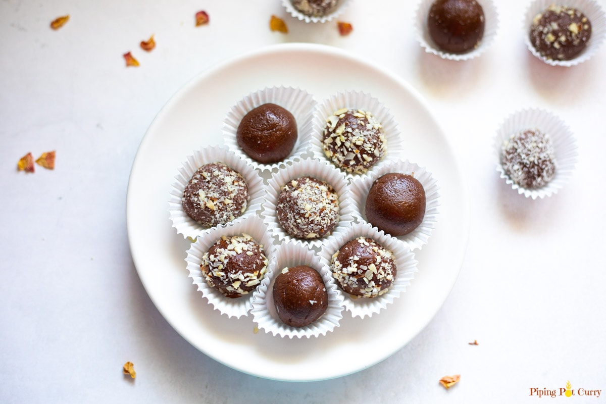 Chocolate balls covered in some chopped nuts in a white plate and spread around.