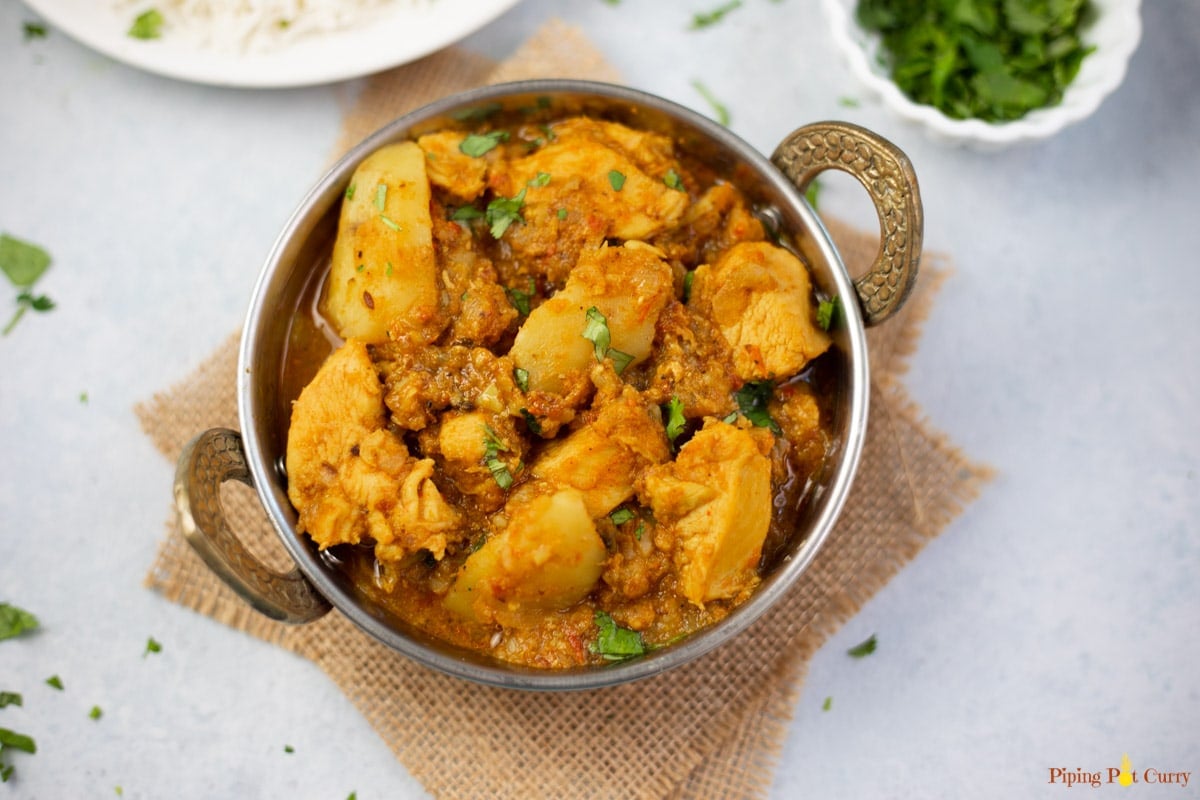 Chicken potato curry in a copper bowl with rice and cilantro in other bowls.