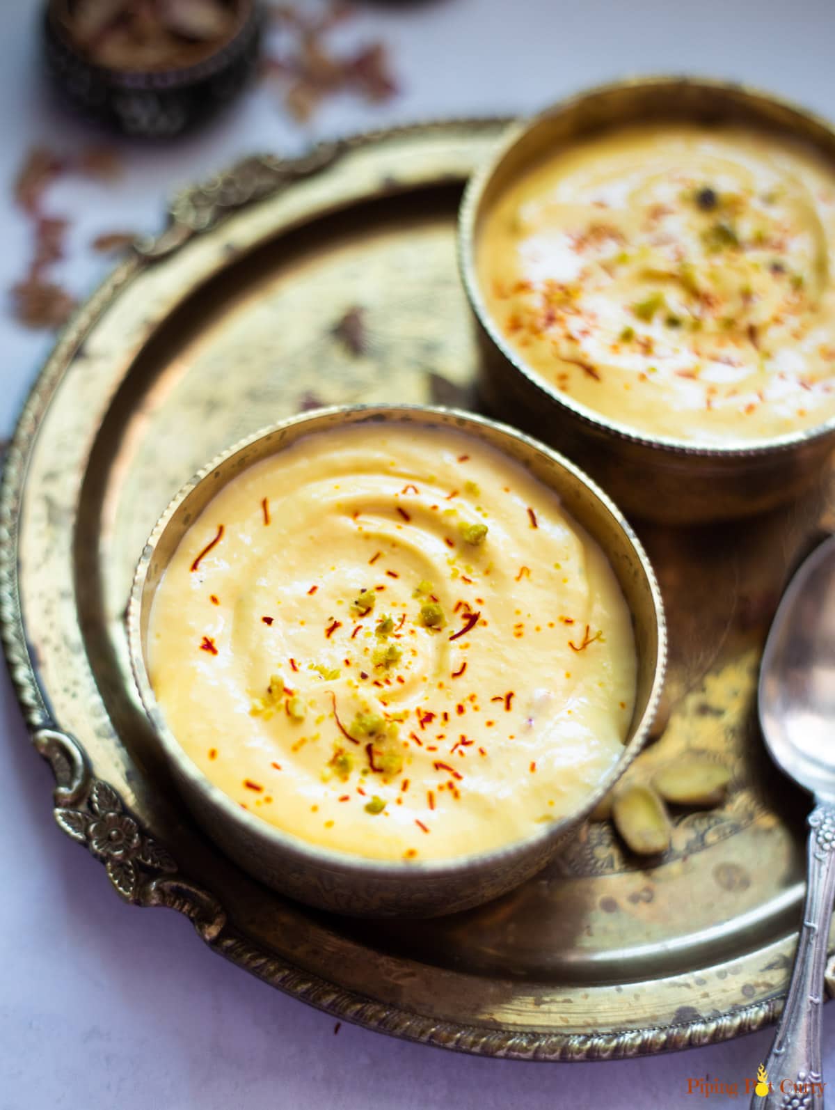Closeup of mango amrakhand (shrikhand dessert) in 2 bowls garnished with saffron on a decorated plate
