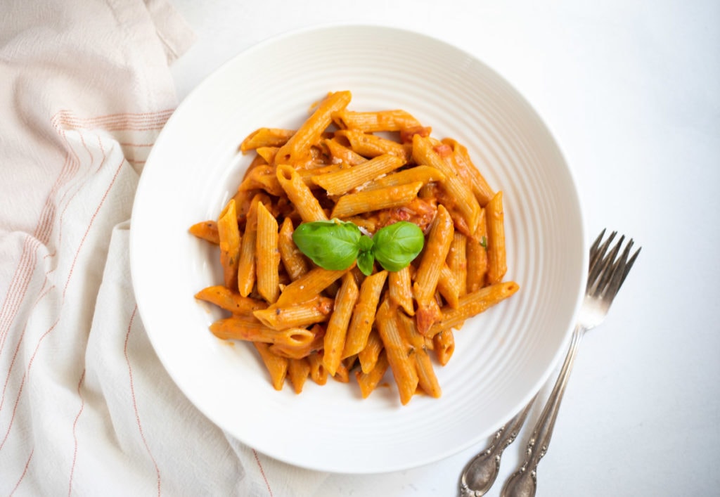 penne pasta in red sauce garnished with basil leaves in a white bowl