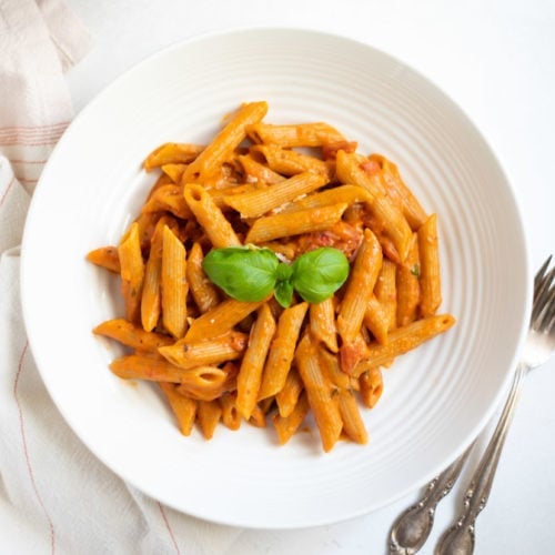 penne pasta in red sauce garnished with basil leaves in a white bowl