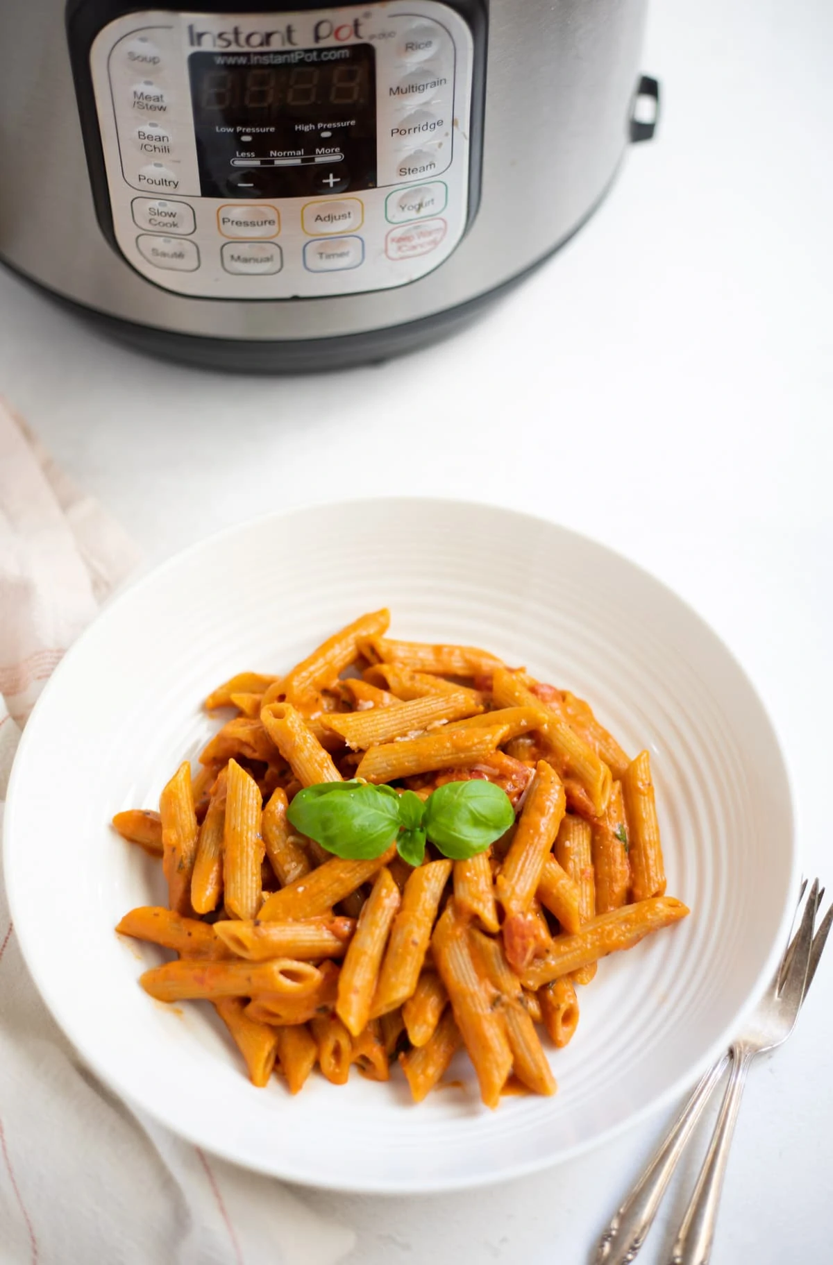 Penne Pasta in Tomato Cream Sauce in a white bowl placed in front of the Instant Pot