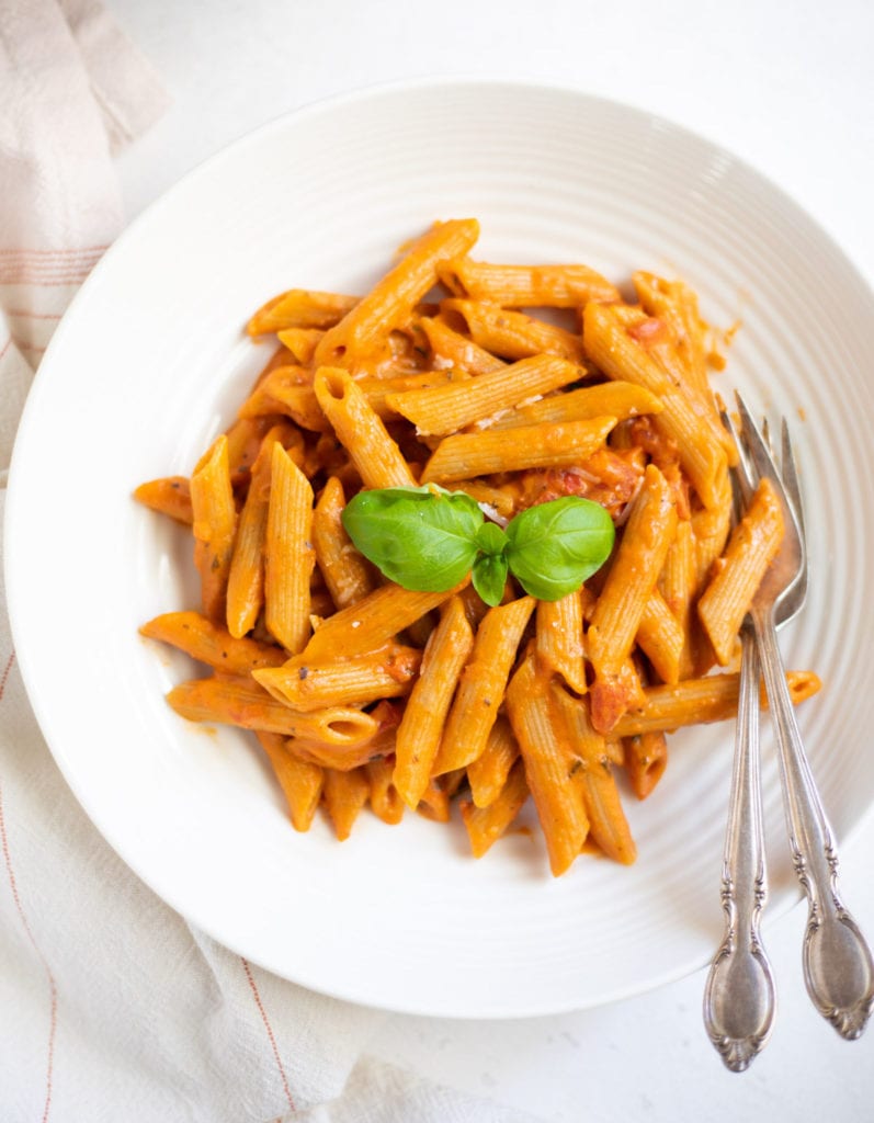 Penne pasta in red tomato sauce in a white bowl garnished with basil leaves