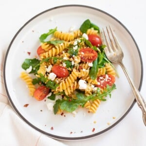 Rotini Chickpea Pasta garnished with arugula in a white plate with silver fork