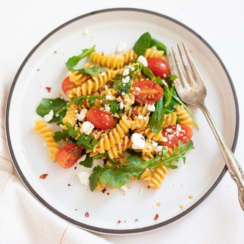 Rotini chickpea pasta salad in a plate topped with feta and crushed red pepper. 