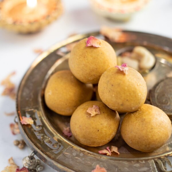 Homemade besan ladoo in a pretty silver plate with Diwali diya's in the back