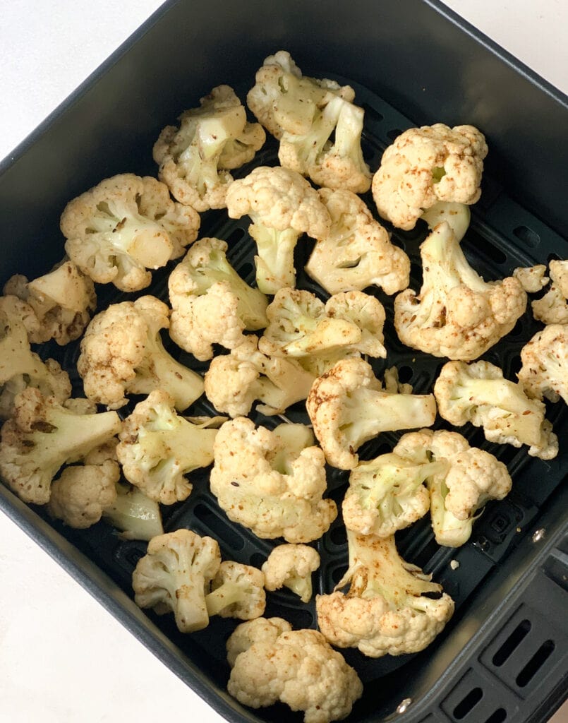 cauliflower mixed with oil and spices in an air fryer basket