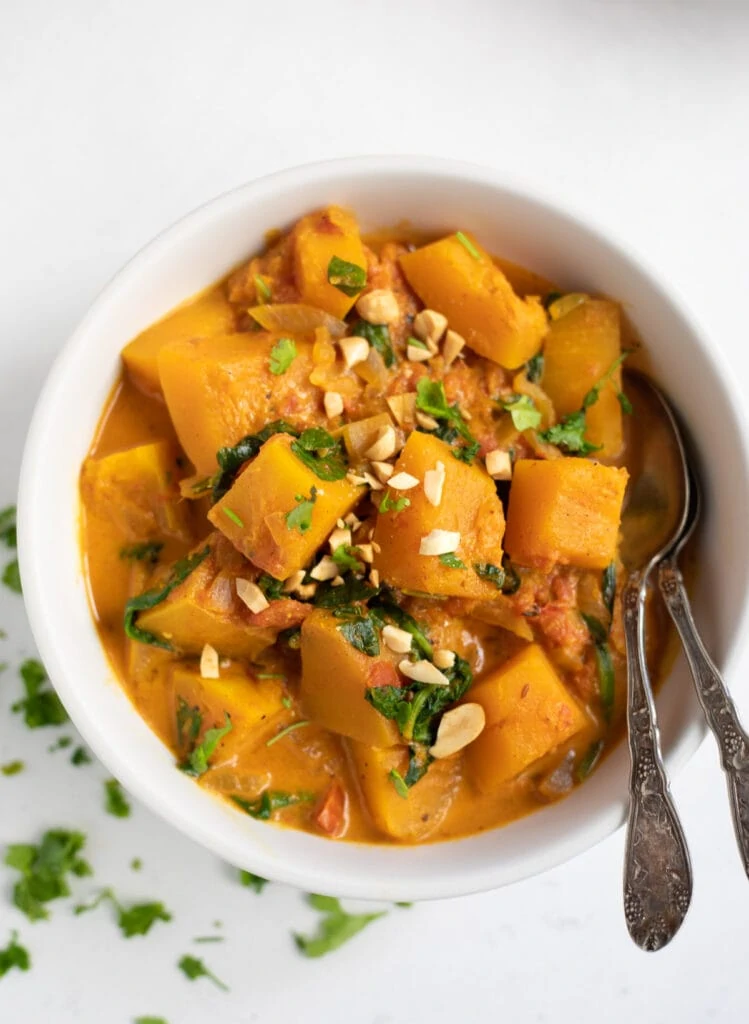 Butternut squash coconut curry topped with cilantro and peanuts in a white bowl