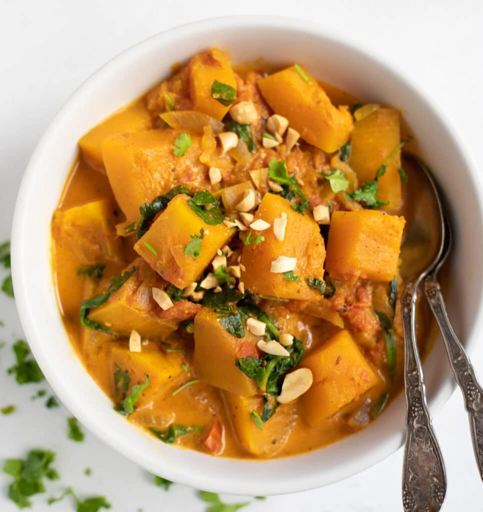 Butternut squash spinach curry topped with cilantro and peanuts in a white bowl