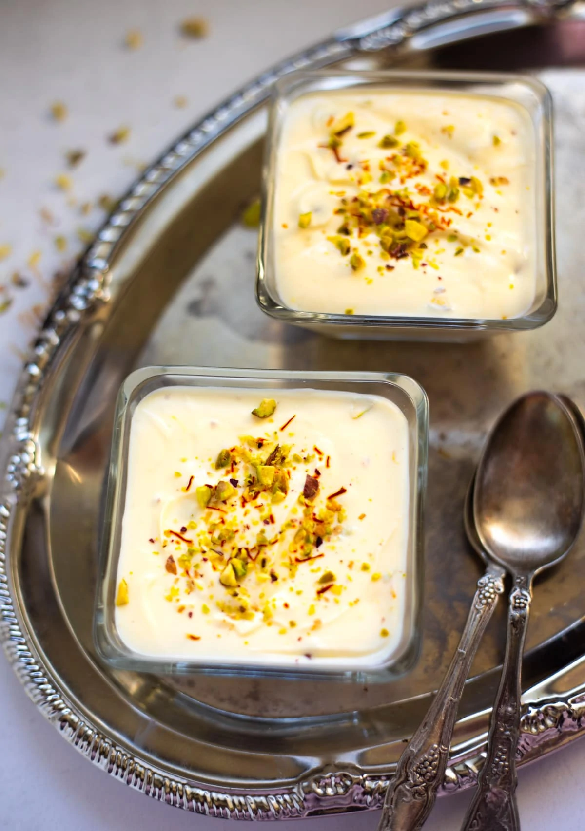 Shrikhand with elaichi and kesar served in pretty bowls in a silver tray 