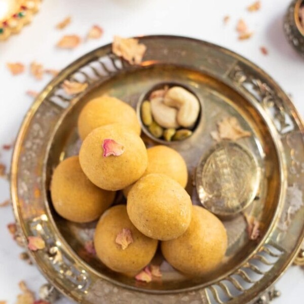 Homemade besan ladoo in a pretty silver plate with Diwali diya's in the back