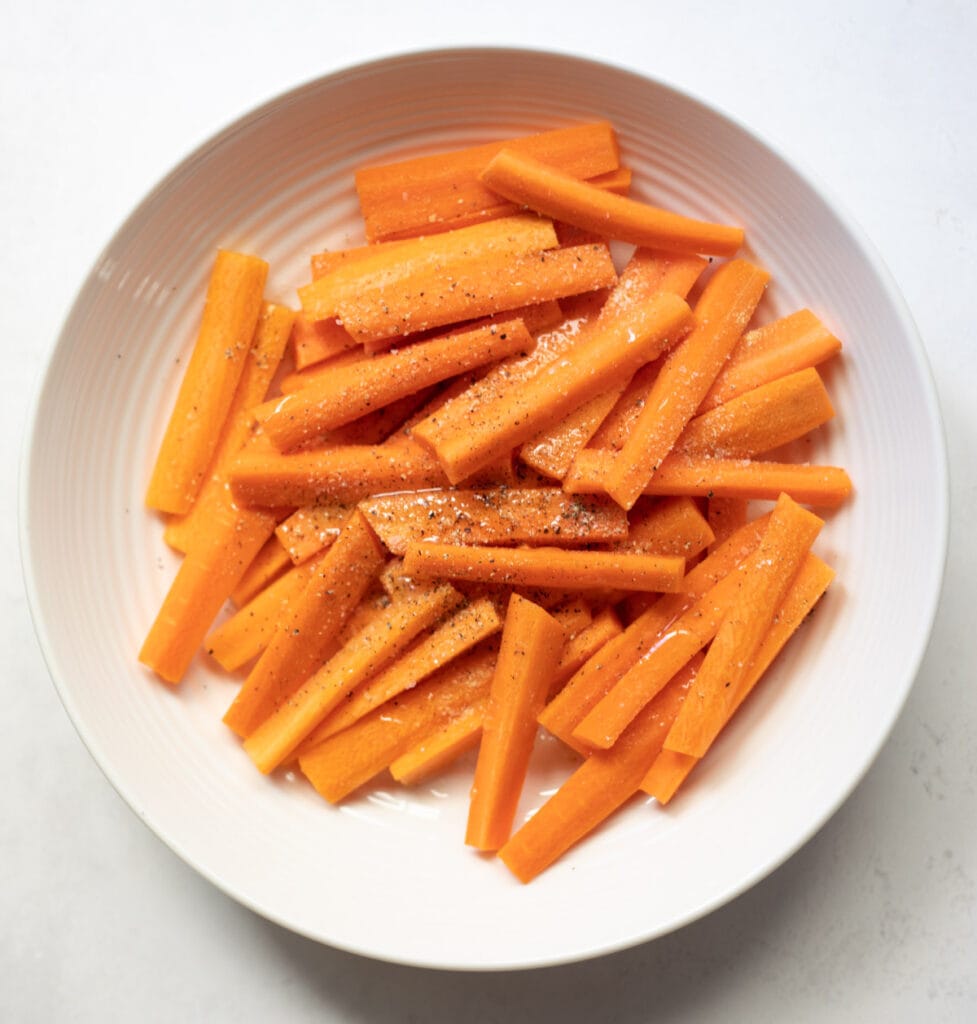 Seasoning carrots in a white bowl