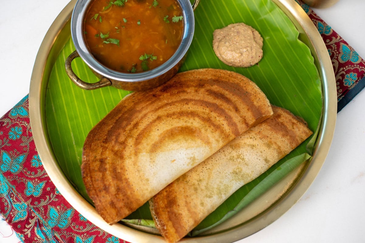 Dosa served with sambar and chutney in a brass plate
