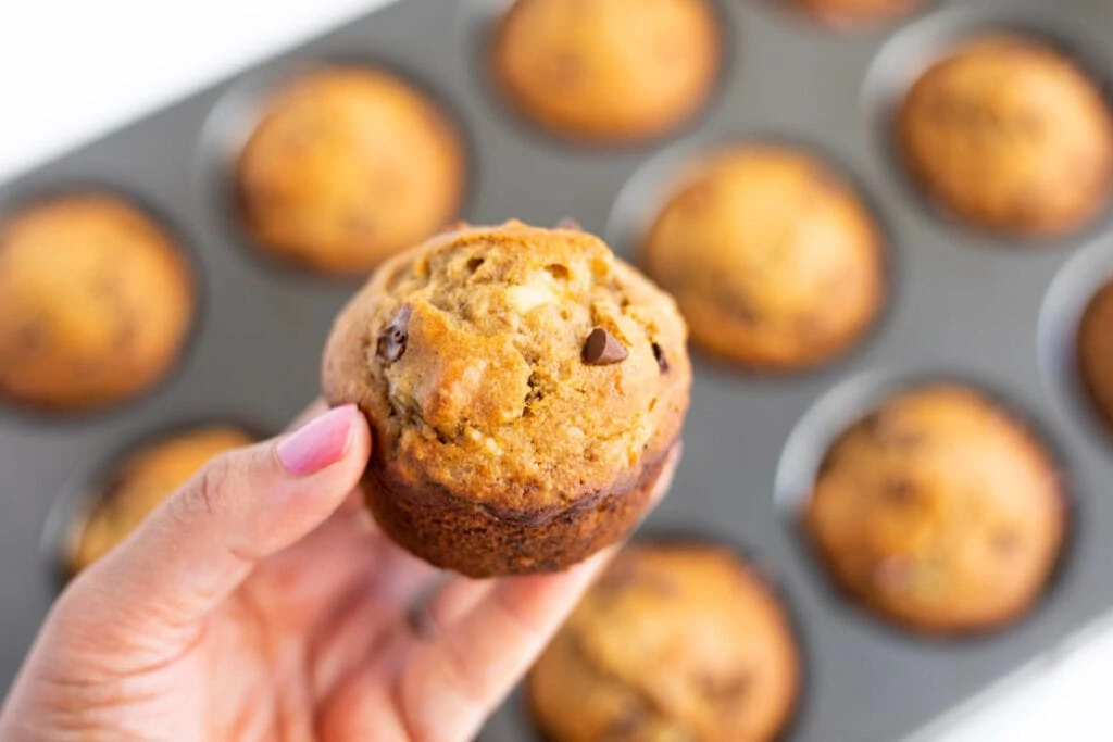 Closeup of a muffin in hand In front of a baking tray full of healthy muffins 