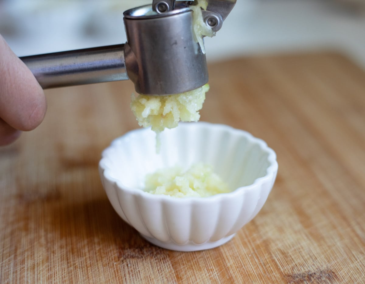 Garlic being minced using a garlic press 