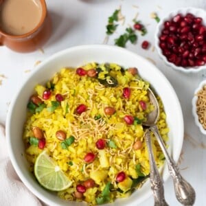 Poha garnished with peanuts and pomegranate in a white bowl with 2 cups of chai