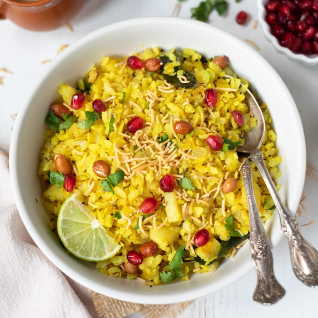 Poha garnished with lemon, sev, cilantro and pomegranate seeds