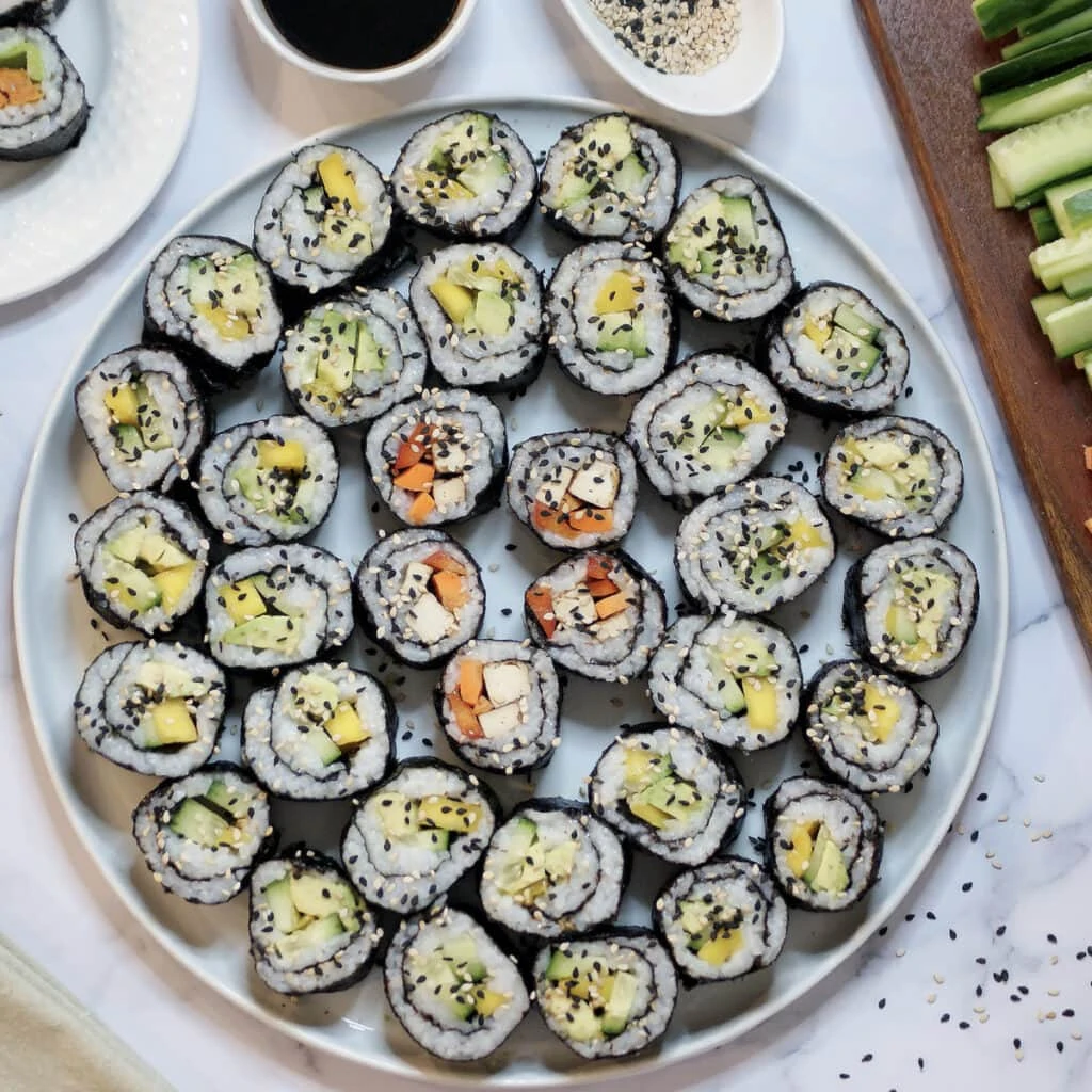 sushi rolls garnished with sesame seeds in a white plate with dip on top