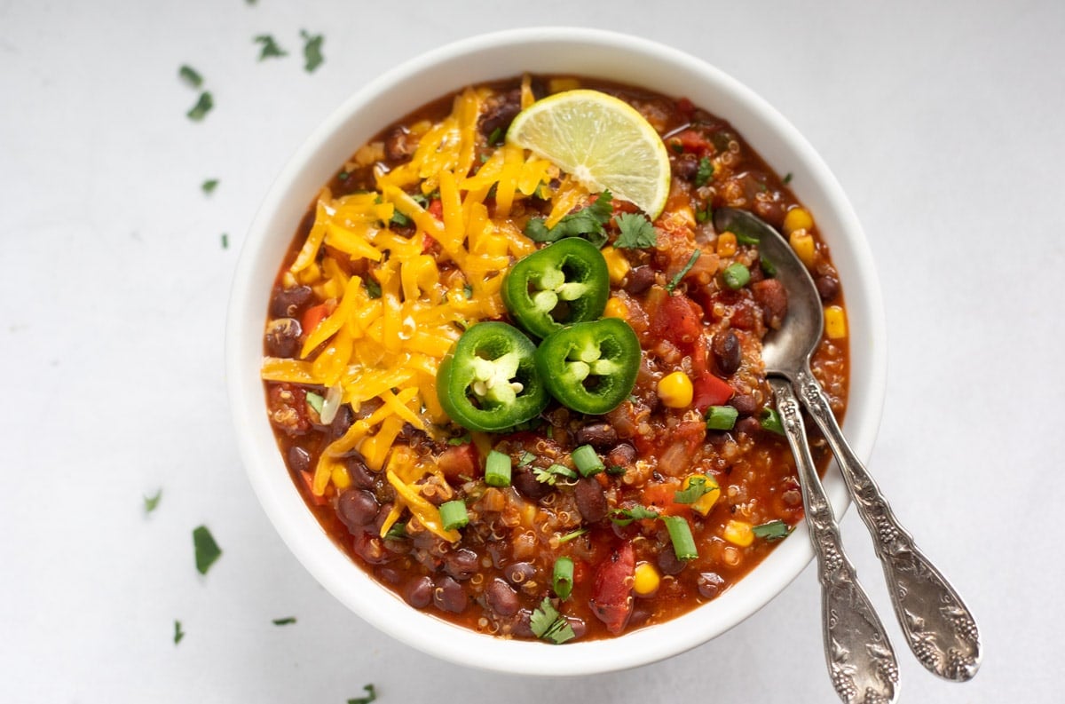 a bowl of vegan quinoa chili with quinoa and black beans topped with cheese, jalapeños and lime