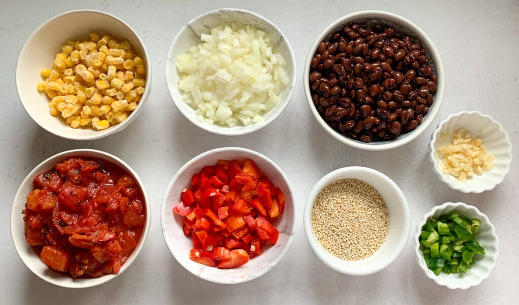 Ingredients such as quinoa, onions, peppers, tomatoes, black beans and corn in small bowls 