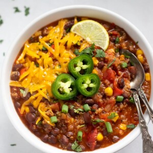 a bowl of vegan chili with quinoa and black beans topped with cheese, jalapeños and lime