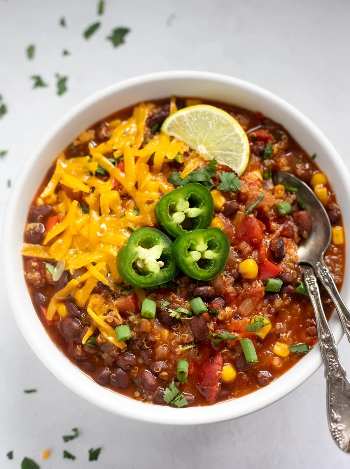 a bowl of vegan chili with quinoa and black beans topped with cheese, jalapeños and lime 