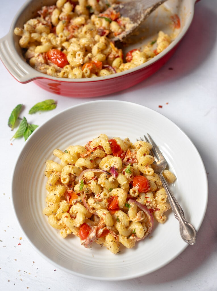 macaroni noodles on a white plate with cherry tomatoes a fork and baking pan in the background